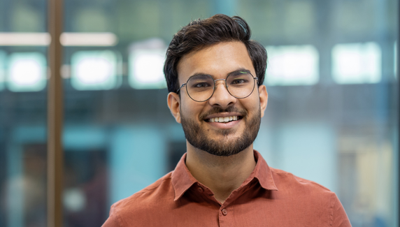 Smiling man wearing glasses in a modern office, with soft graphic shapes overlaid.