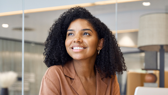 Smiling woman with curly hair in a modern office, looking to the side, with soft pastel graphic shapes overlaid.